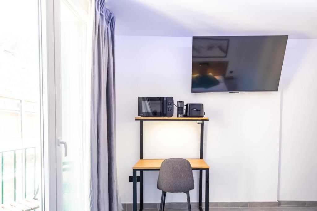 A room with a desk, a chair, a flat-screen TV mounted on the wall, and a window with curtains.