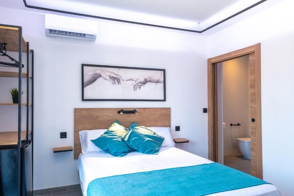 A modern bedroom with a bed, a framed artwork above it, and a wooden door leading to a bathroom.