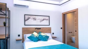 A modern bedroom with a bed, a framed artwork above it, and a wooden door leading to a bathroom.