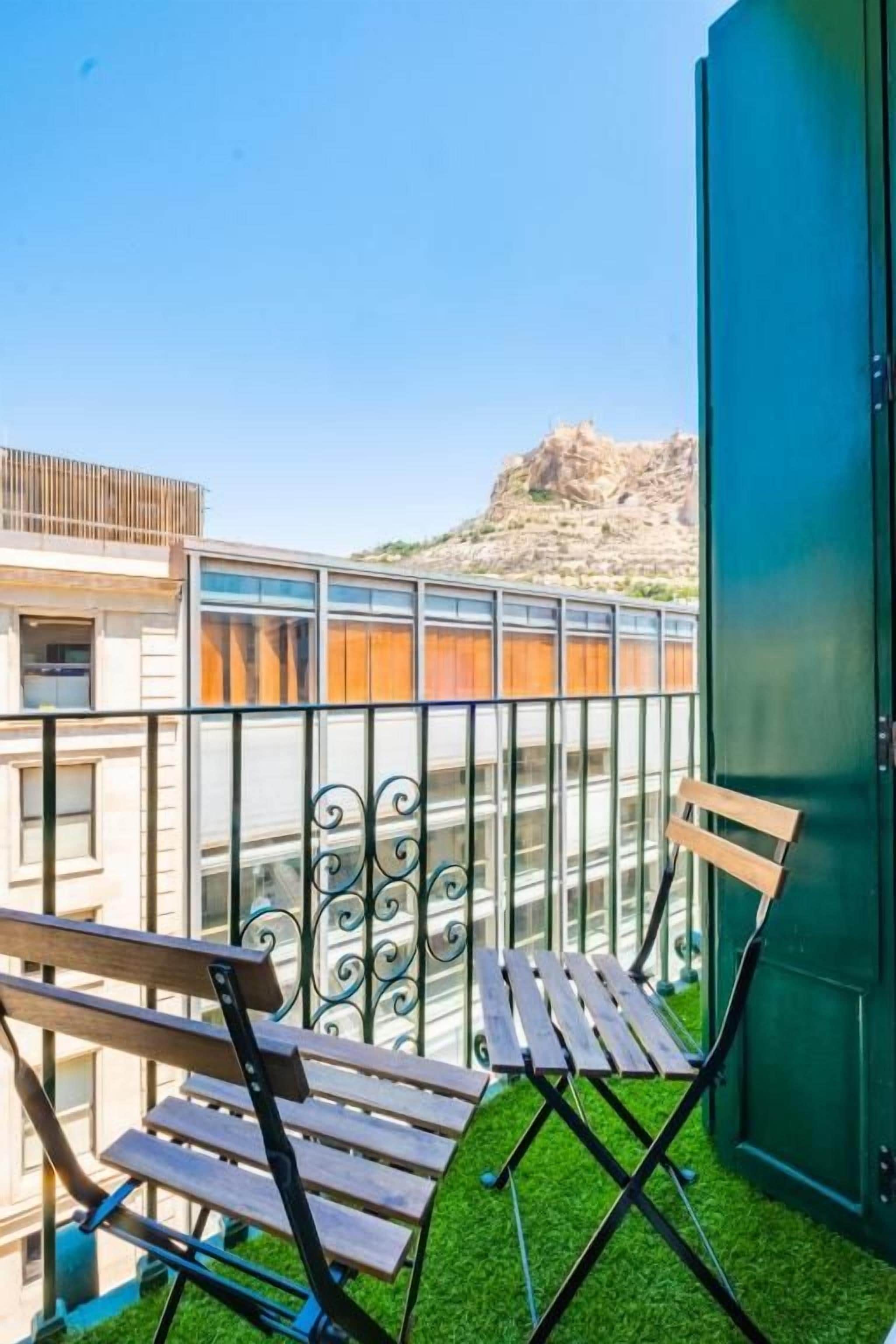 Un balcón con un banco de madera, una puerta verde y vistas a un paisaje rocoso.