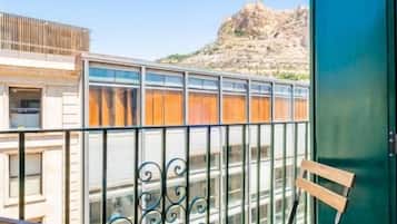 Un balcón con un banco de madera, una puerta verde y vistas a un paisaje rocoso.