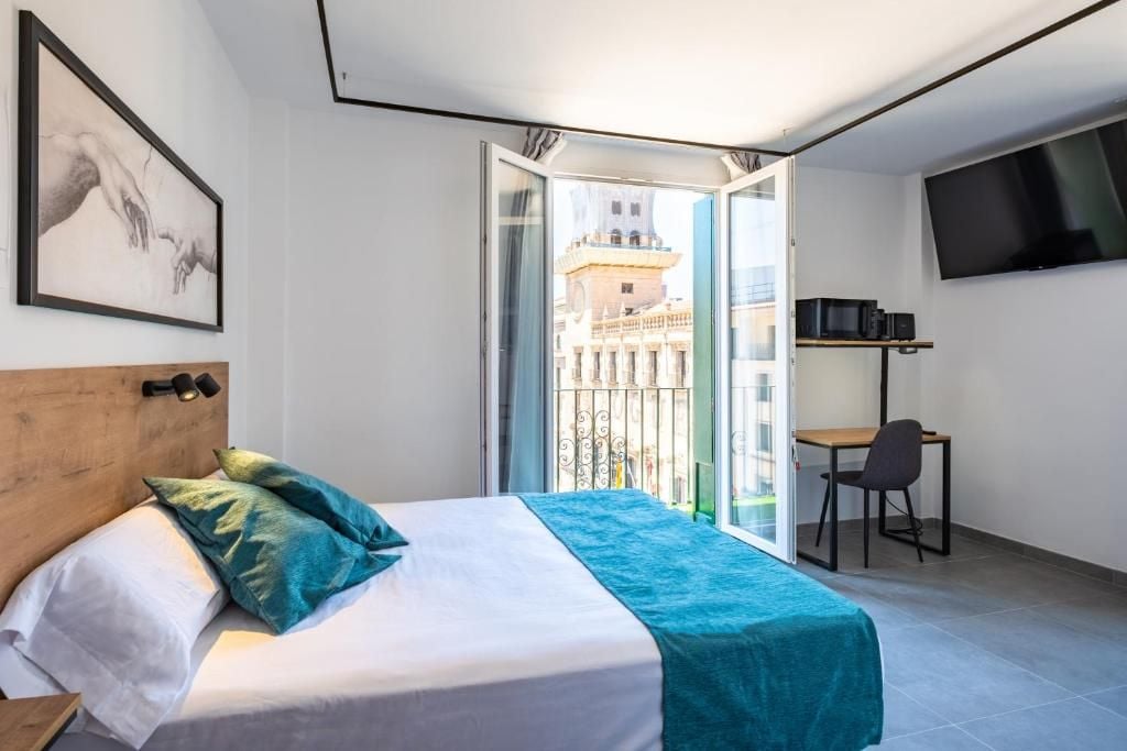A hotel room with a bed, a desk, a chair, a TV, and a balcony with a city view.