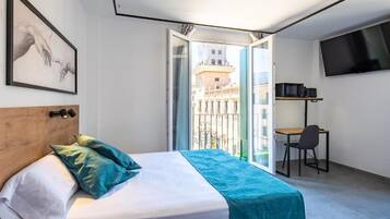 A hotel room with a bed, a desk, a chair, a TV, and a balcony with a city view.