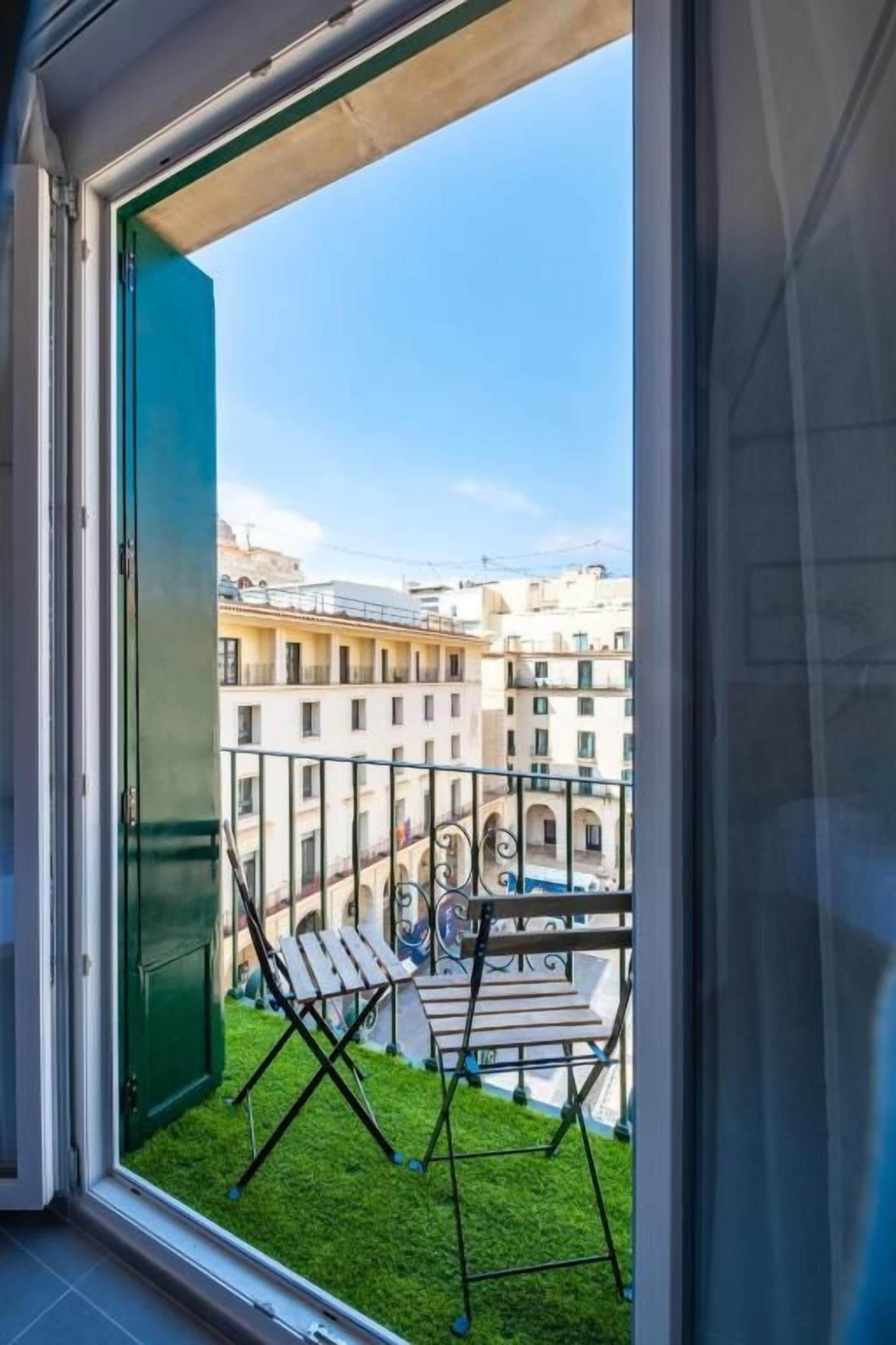 Un balcón con vista a un paisaje urbano, una puerta verde y una barandilla de metal.