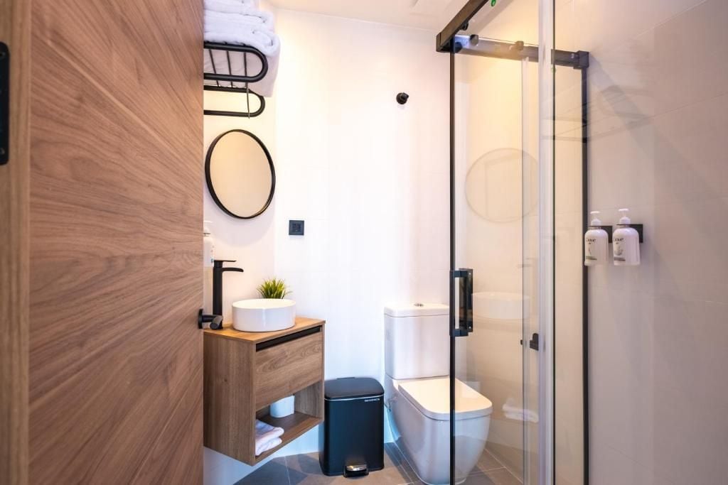 A modern bathroom with a wooden vanity, a toilet, a glass shower enclosure, and a small plant on the vanity.