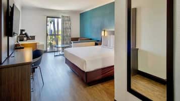 A hotel room with a bed, desk, chair, and a view of the outdoors.