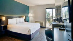 Une chambre d’hôtel comprenant un lit, des tables de chevet, un bureau, une chaise, une lampe et une grande fenêtre.