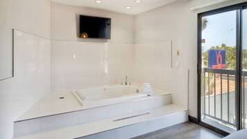 A modern bathroom with a large bathtub, a small window, and a balcony with a view.