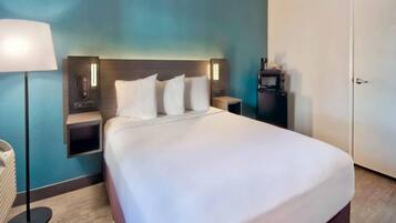 A hotel room with a large bed, bedside tables, a lamp, and a minibar.