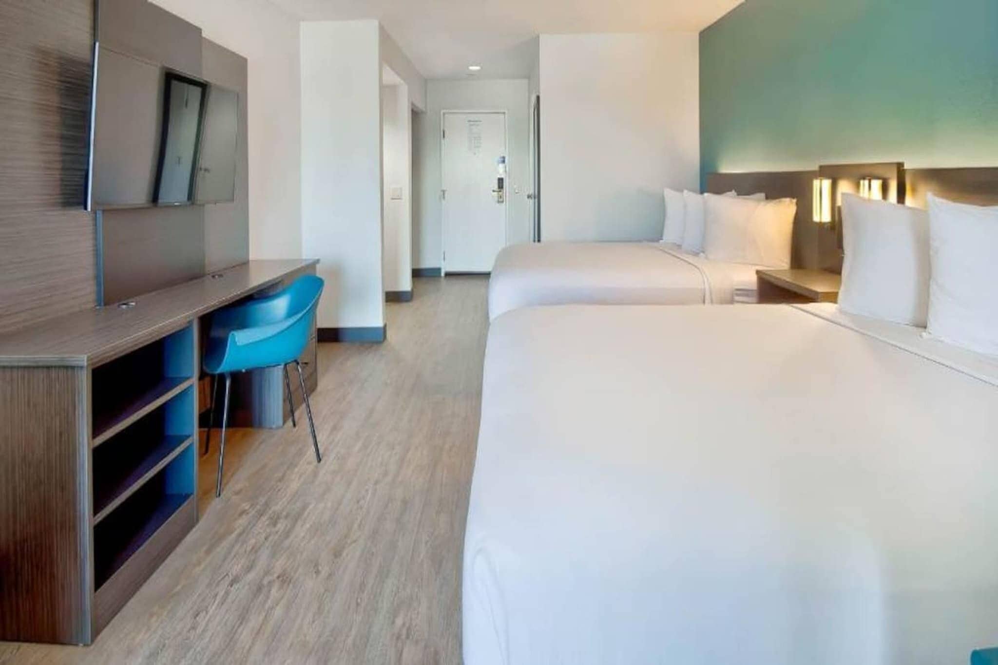 A hotel room with a bed, a desk, a chair, and a television.