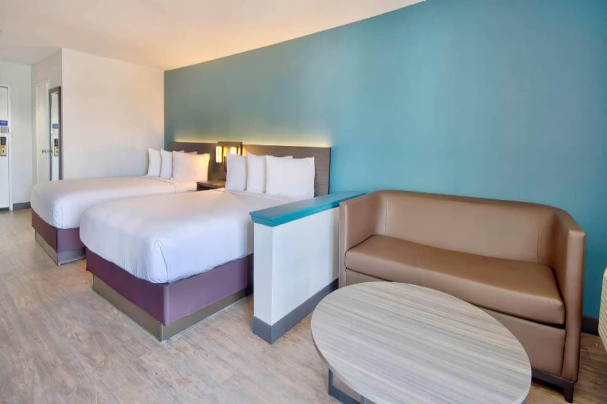 Ein Hotelzimmer mit zwei Betten, einer Couch, einem kleinen Tisch und einer blauen Wand.