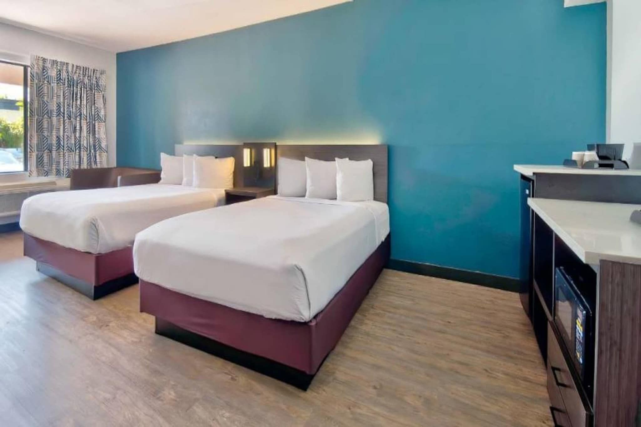 A hotel room with two beds, a desk, and a view of the outdoors.