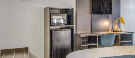 A hotel room with a bed, a desk, a refrigerator, and a television.