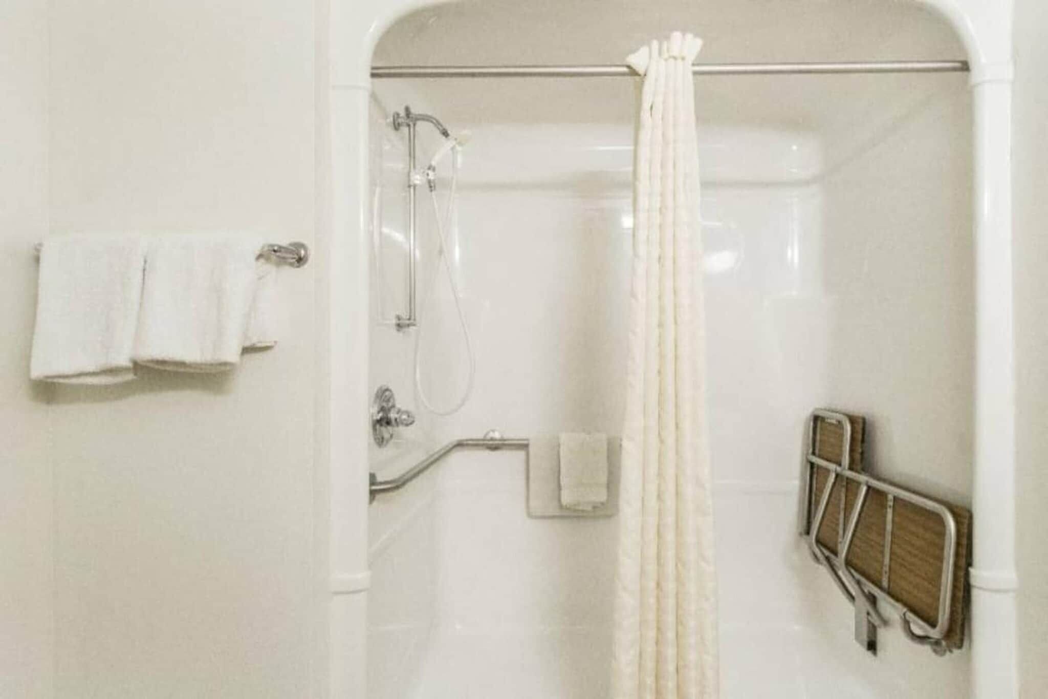 A shower area with a glass door, a towel rack with two towels, a shower control panel, and a safety grab bar.