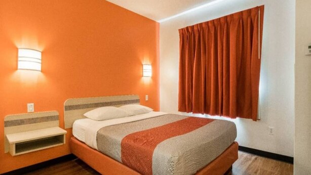 Een hotelkamer met een bed, nachtkastjes, een raam met gordijnen en wandlampen.