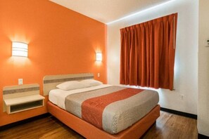 A hotel room with a bed, bedside tables, a window with curtains, and wall-mounted lights.