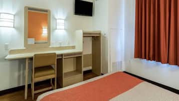 A hotel room with a bed, a desk, a chair, a mirror, a television, and a wardrobe.
