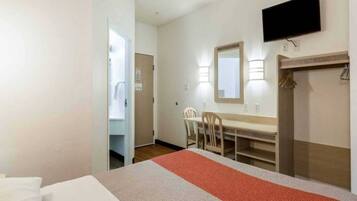 A hotel room with a bed, a desk with chairs, a television, and a wardrobe.