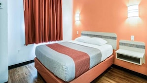 Een hotelkamer met een bed, nachtkastje, raam met gordijnen en wandlampen.