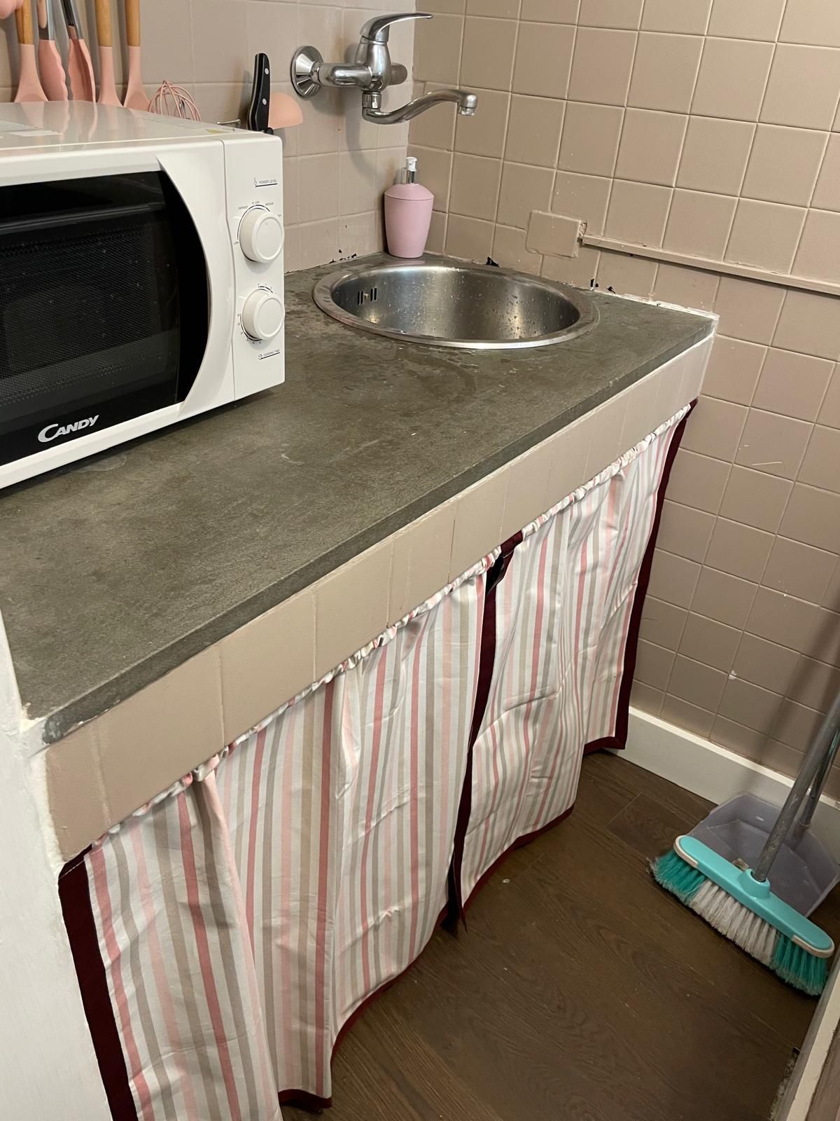 A kitchen with a microwave, sink, and striped curtains.