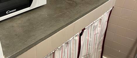 A kitchen with a microwave, sink, and striped curtains.