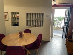 A dining area with a round wooden table, red chairs, and shelves with glassware and kitchen items. - The Burgundy Nest near Campo de Fiori (Roma)