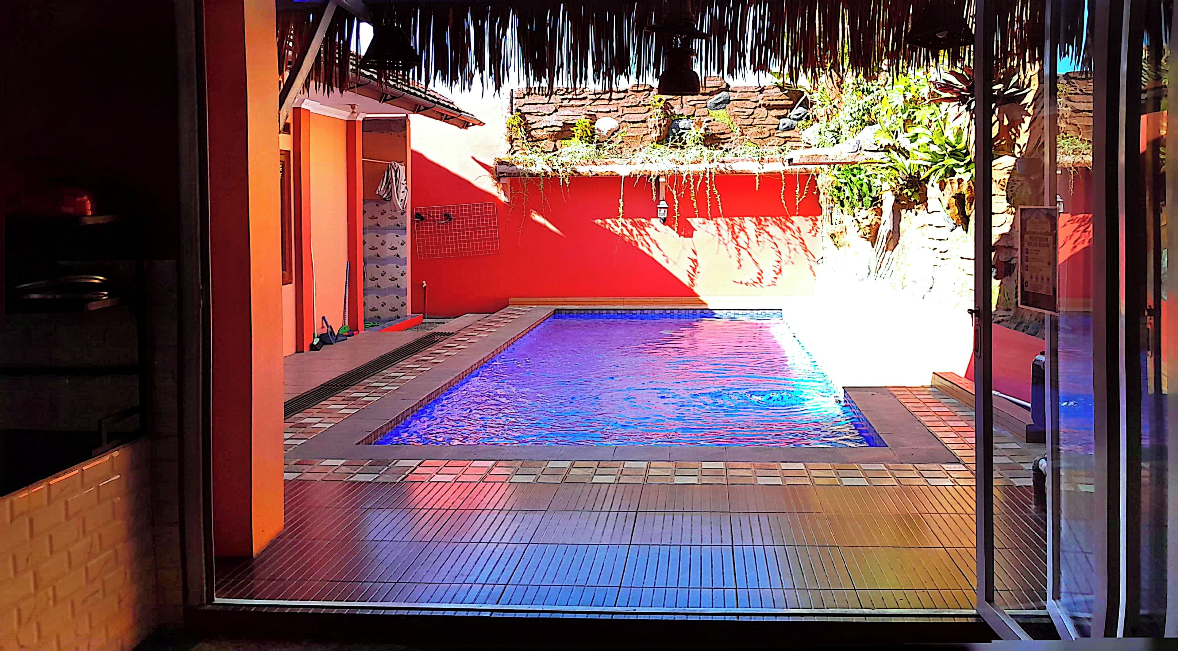 Una piscina con borde de baldosas, rodeada por un muro rojo y una estructura de piedra.