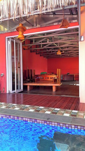 A room with a red wall, a wooden bed, a window, and a pool area. - Villa Dinar Strawberry (Bandung Barat)