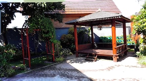 Un mirador de madera con techo de tejas, rodeado de follaje y un muro de ladrillo.