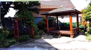 Un mirador de madera con techo de tejas, rodeado de follaje y un muro de ladrillo.