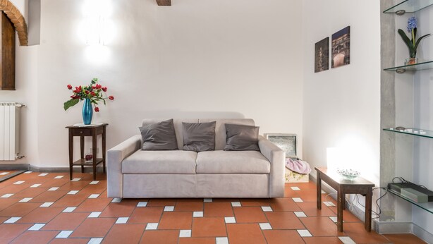 Un soggiorno con un divano color beige, un tavolino con un vaso di fiori e un pavimento piastrellato.