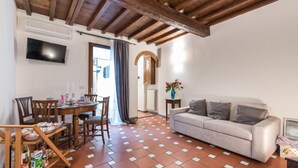 Un soggiorno con divano, tavolo da pranzo con sedie, TV a parete e pavimento piastrellato.