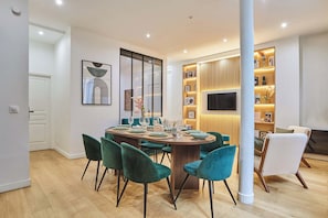 A modern dining area with a round table, teal chairs, and a TV mounted on the wall. - Superb apartment for 8 people - Sacré Coeur (Paris)