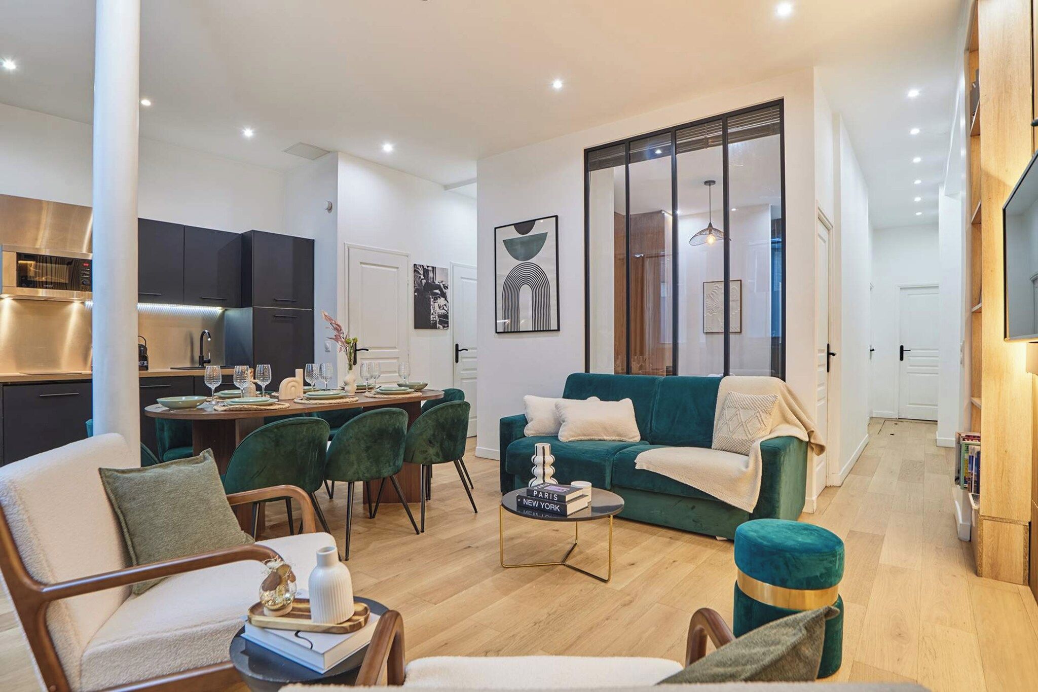 A modern living room with a dining area, a kitchen in the background, and a large window with a view.