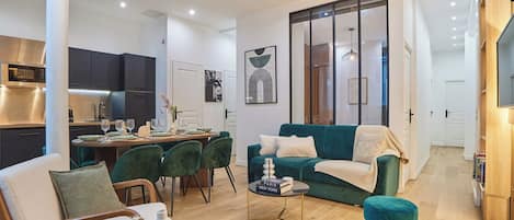 A modern living room with a dining area, a kitchen in the background, and a large window with a view.