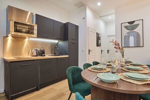 A modern kitchen with dark cabinets, a stainless steel range hood, and a dining area with a round table set for six. - Superb apartment for 8 people - Sacré Coeur (Paris)