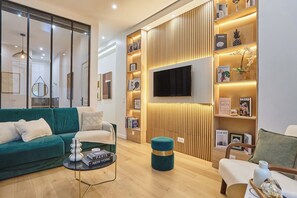 A modern living room with a teal sofa, a coffee table, a TV mounted on a wooden wall, and a bookshelf with magazines. - Superb apartment for 8 people - Sacré Coeur (Paris)
