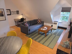 A modern living room with a gray sofa, yellow chairs, a wooden coffee table, and a view of the outdoors through a window. - The Loft in Golden | Downtown · King Bed (Golden)