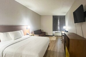 Et hotelværelse med en stor seng, et skrivebord, en stol og et fjernsyn på væggen.