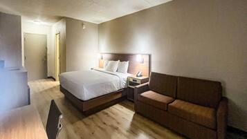 A hotel room with a bed, a bedside table with a phone, a sofa, and a wooden floor.