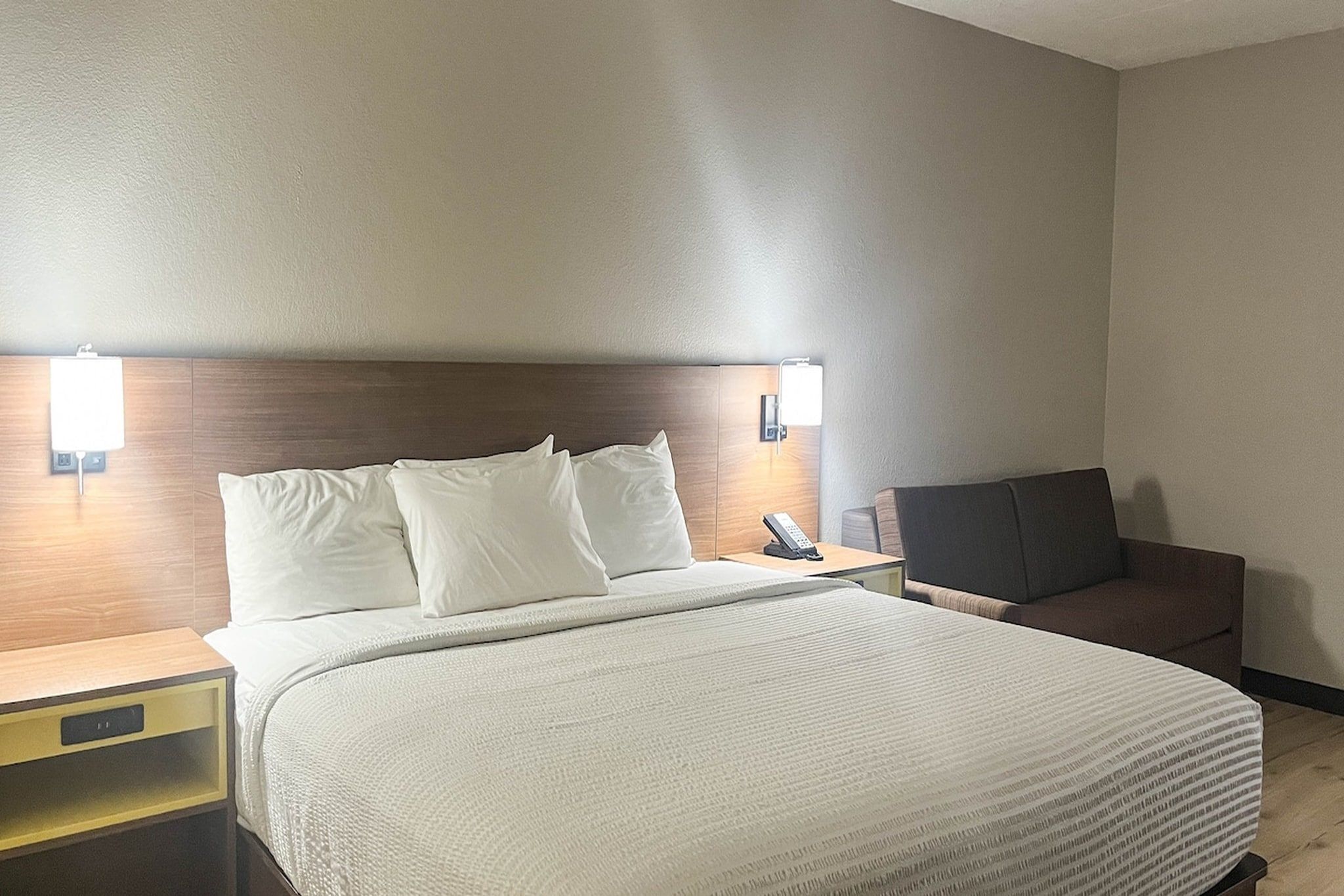 Una habitación de hotel con cama, mesitas de noche, una silla y lámparas fijadas a la pared.