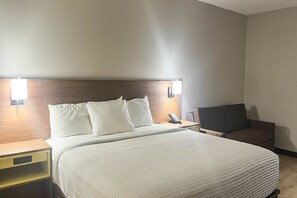 A hotel room with a bed, bedside tables, a chair, and wall-mounted lights.