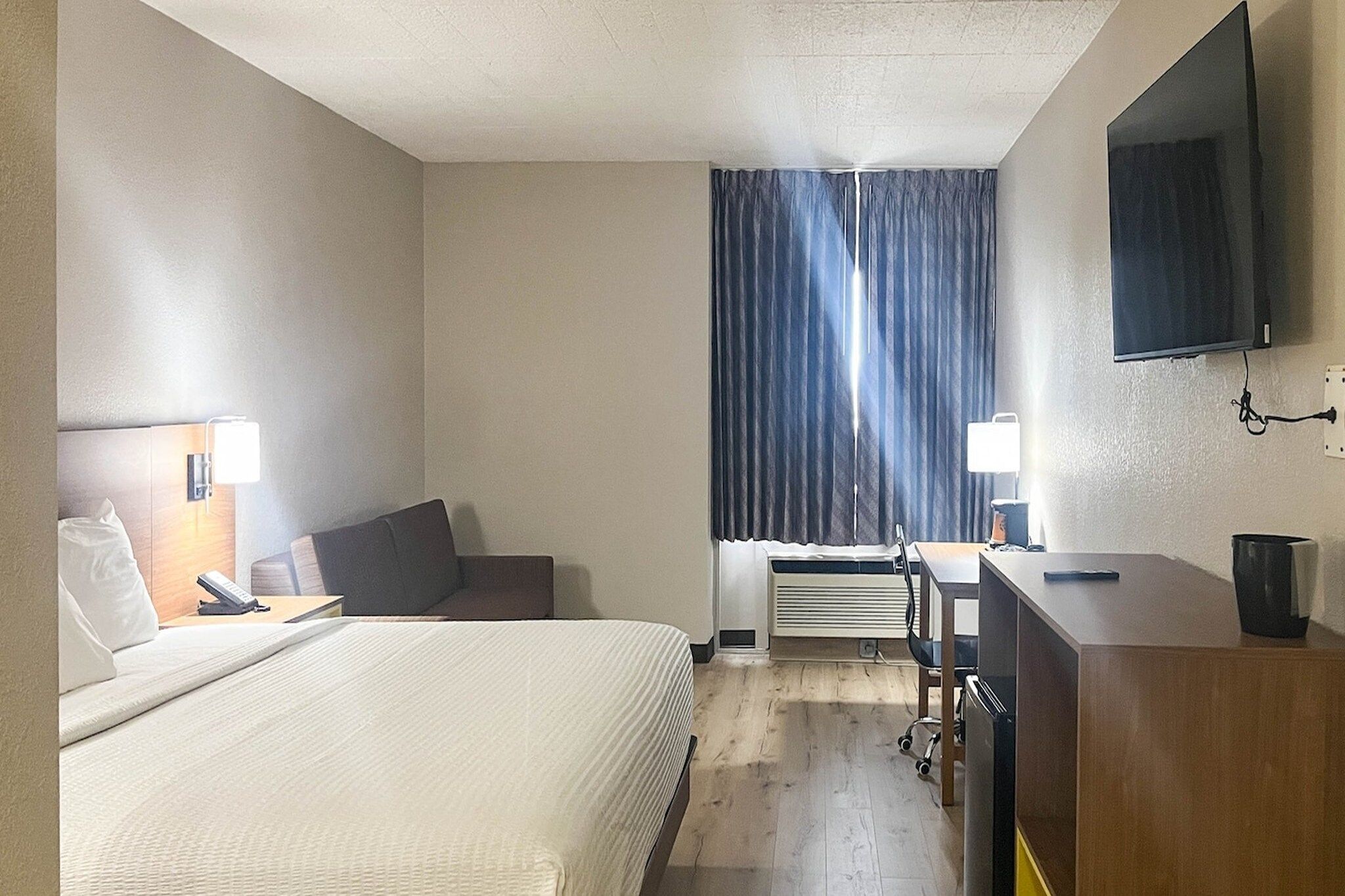 Une chambre d’hôtel équipée d’un lit, d’un bureau, d’une chaise, d’une télévision et d’une fenêtre avec des rideaux.