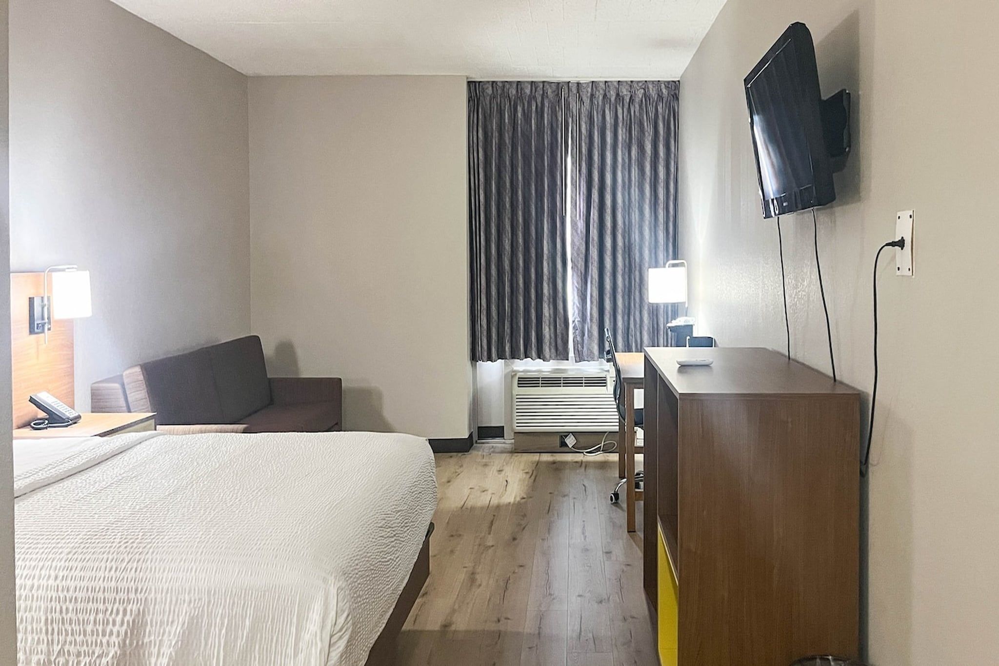 A hotel room with a bed, a desk, a chair, a television, and a window with curtains.