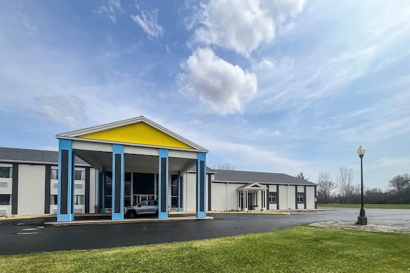 A building with a covered entrance, a parking lot, and a grassy area.