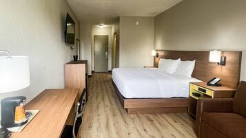 A hotel room with a bed, bedside tables, a desk, a chair, a TV, and a door leading to a hallway.