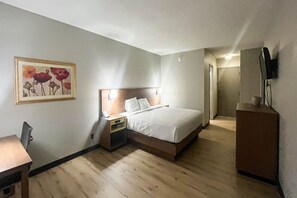 Une chambre d’hôtel avec un lit, une table de chevet, une chaise, un bureau et un tableau au mur.