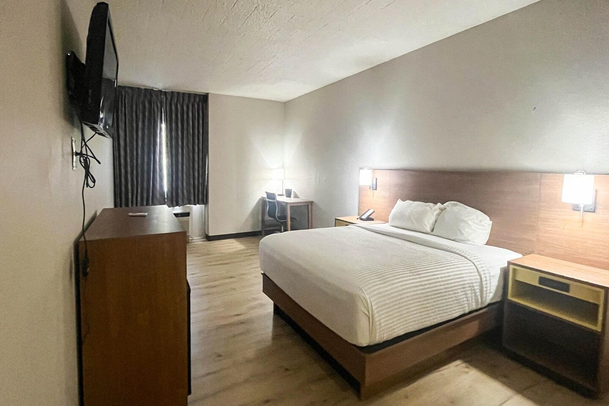 Una habitación de hotel con cama, mesitas de noche, escritorio, silla y televisor montado en la pared.
