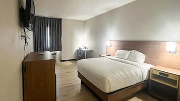 Una habitación de hotel con cama, mesitas de noche, escritorio, silla y televisor montado en la pared.
