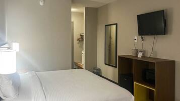 A hotel room with a bed, a television mounted on the wall, a small desk with a chair, and a mirror.